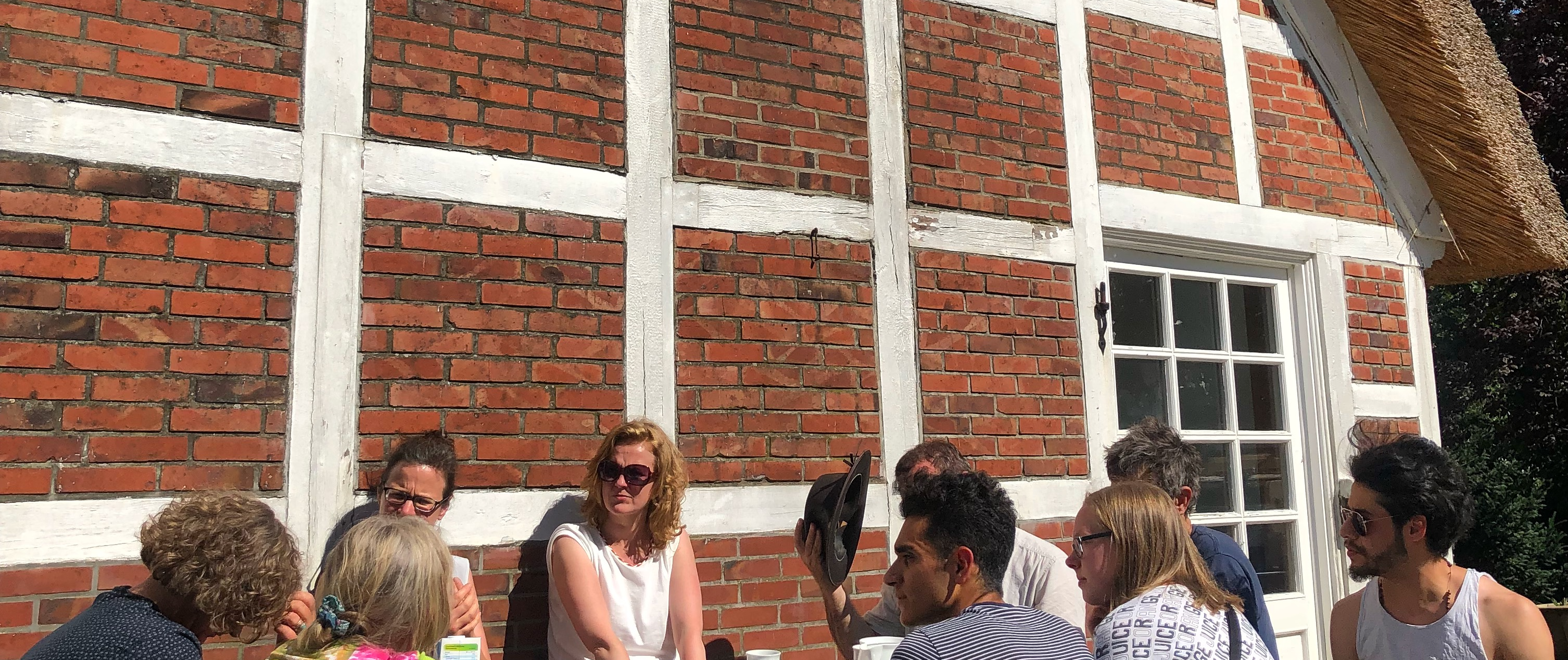 Menschen sitzen im Sonnenschein vor dem Fachwerk des ABCs.